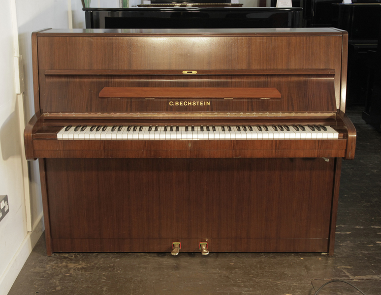 A 1988, Bechstein upright piano with a walnut case. Piano has an eighty-eight note keyboard and two pedals.