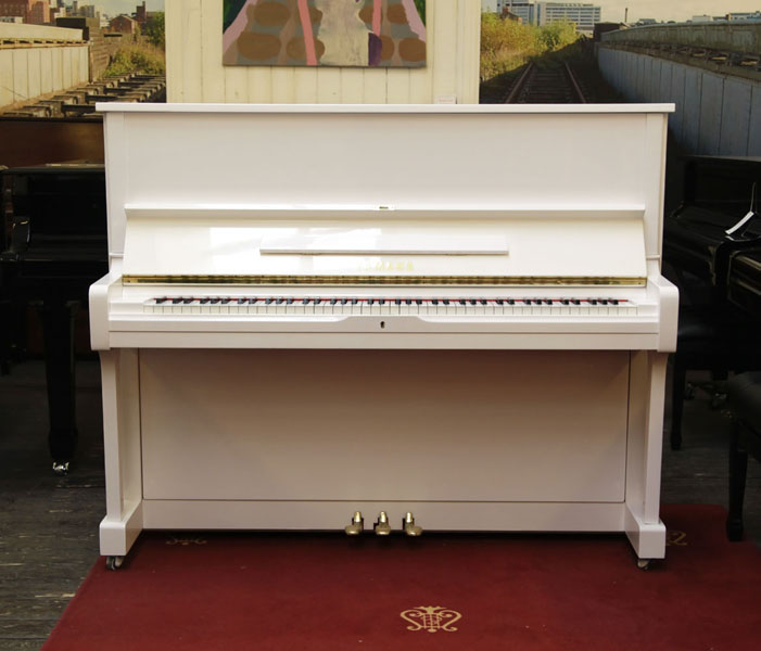 A 1986, Yamaha U1A upright piano with a white case and polyester finish. Piano has an eighty-eight note keyboard and three pedals.