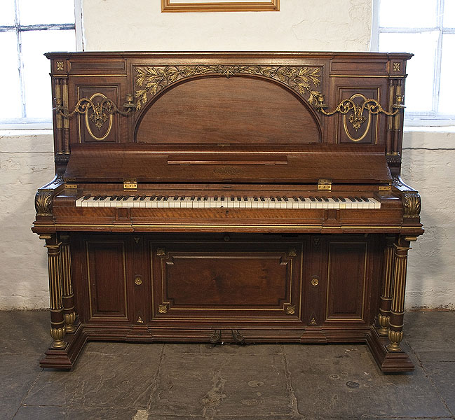 An 1892, Erard upright piano with a Renaissance style walnut case with gilt accents. Cabinet features ancient Roman elements including doric columns, rosettes and a front panel carved with myrtle.