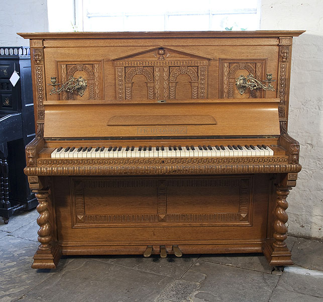 A Helmholz upright piano for sale with a Romanesque style, oak case and barley twist legs. Cabinet features a front panel ornately carved with rounded arches and grotesque heads on piano cheeks.