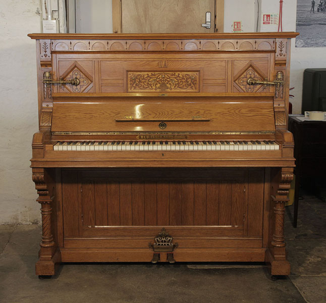An 1895, English Gothic style, Ibach upright piano with a carved, oak case and ornate brass candlesticks and handles. Cabinet features traditional folk art motif carvings.  Piano has an eighty-five note keyboard and two pedals. 