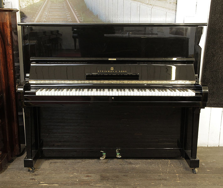 A 1961, Steinway Model V upright piano with a black case and brass fittings. Piano has an eighty-eight note keyboard and two pedals.