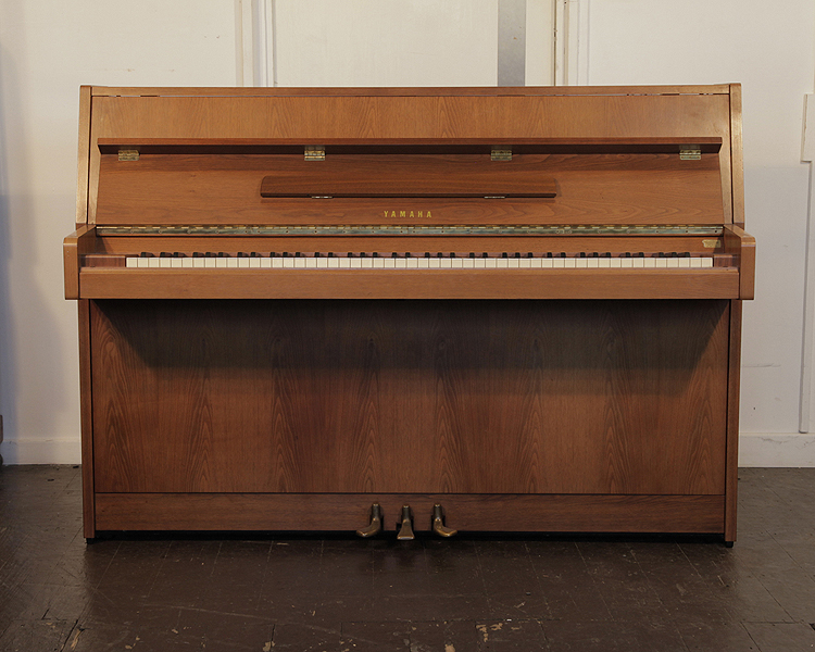 A 1980, Yamaha M5J upright piano with a satin, walnut case. Piano has an eighty-eight note keyboard and three pedals 