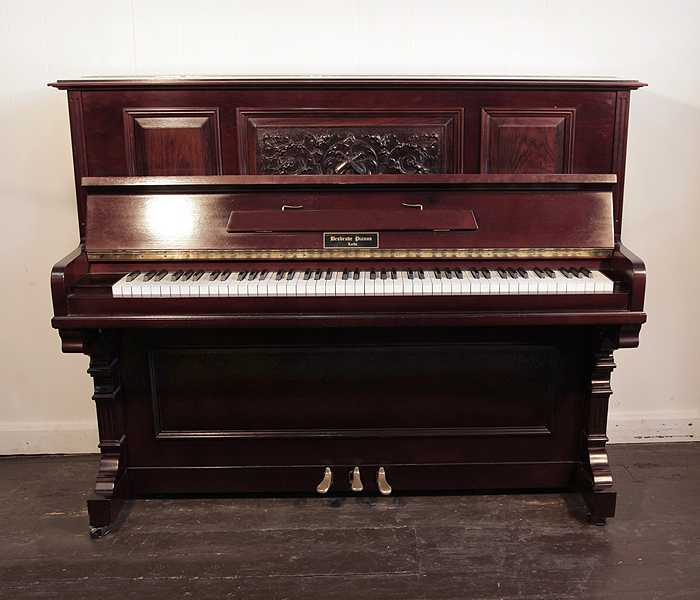 Besbrode upright piano with a mahogany case and carved, front panel in a Neoclassical design. Piano has an eighty-eight note keyboard and three pedals. .