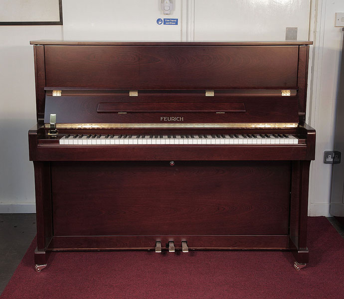 Brand new, Feurich Model 122 upright piano with a satin, walnut case and brass fittings. Piano has an eighty-eight note keyboard and three pedals..