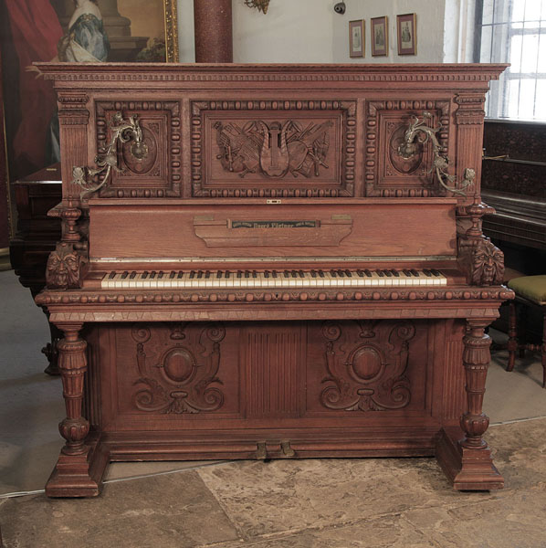 Georg Fortner upright piano for sale with an ornately carved, mahogany case and ornate candlesticks. Cabinet features carved   flowers, foliage, musical instruments   and grotesque heads on each piano cheek. Carvings created by Julius Bechler, wood carver to King Ludwig II.  Piano has an eighty-five note keyboard and two pedals.