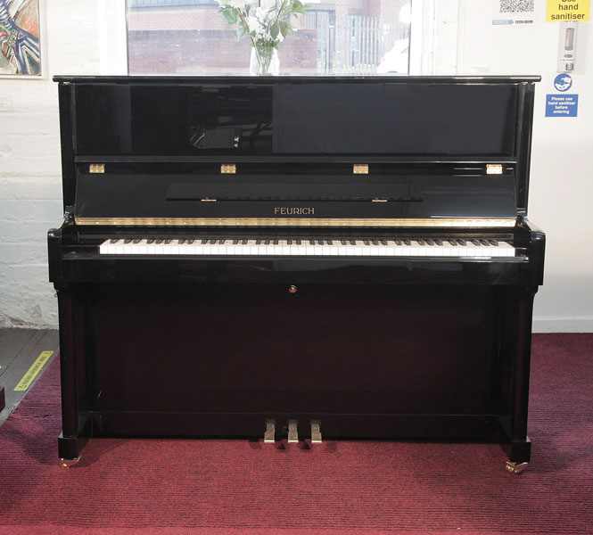 Brand new, Feurich Model 122 upright piano with a black case and brass fittings. Piano has an eighty-eight note keyboard and three pedals..