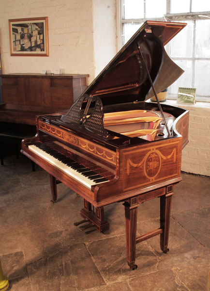Pre-owned,  1903, Broadwood grand piano with a rosewood case and gate legs. Cabinet inlaid with swags, bows and panels of musicl instruments. Piano has an eighty-five note keyboard and two-pedal lyre. 