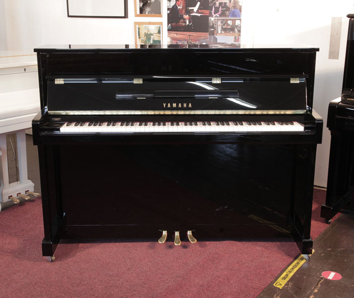 A Yamaha b2e PE  upright piano with a gloss black case and brass fittings. Piano has an eighty-eight note keyboard and three pedals. Condition as new.