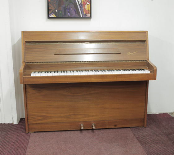 British-Made, 1977, Danemann upright piano with a walnut case and Schwander action. Piano has an eighty-eight note keyboard  and two pedals 