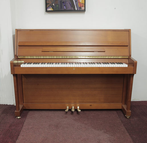 Pre-owned, Steinbach UP108M upright piano with a walnut case. Piano has an eighty-eight note keyboard and three pedals. 