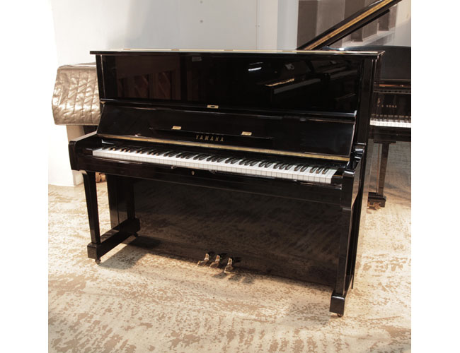  1977, Yamaha U1 upright piano in black gloss with brass fittings. Piano has an eighty-eight note keyboard and three pedals