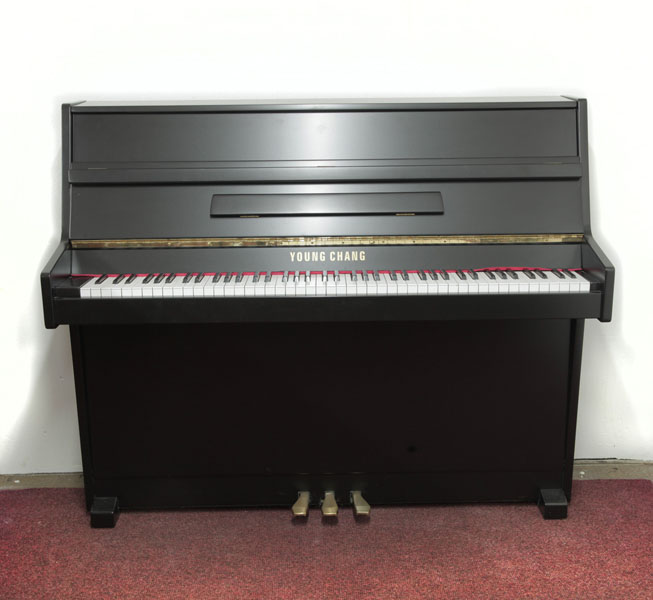 A 1988, Young Chang U-109   upright piano with a satin, black case and brass fittings . Piano has an eighty-five note keyboard and three pedals